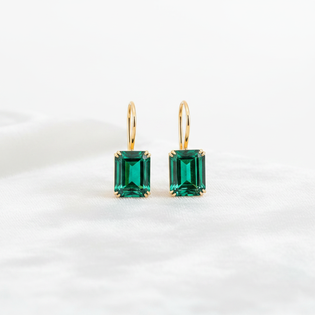 14K gold emerald cut green emerald drop earrings on white velvet, studio lighting