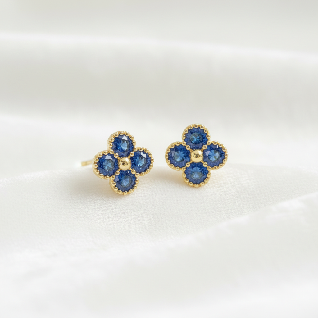 14K gold sapphire flower clover stud earrings on wavy white velvet fabric, studio lighting