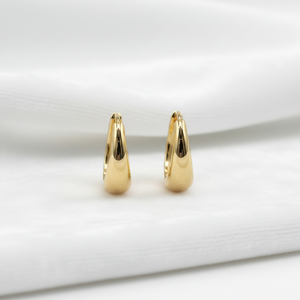 14K gold teardrop tapered huggie hoop earrings on wavy white velvet, studio lighting
